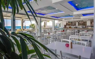 a restaurant with white tables and chairs and the ocean at Island Boutique Hotel in Larnaka