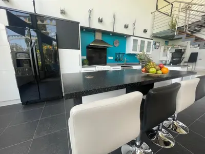 a kitchen with a black counter and white chairs at VILLA CATALEYA Fig Tree Bay Protaras Town Center in Protaras