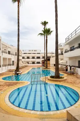 a swimming pool with palm trees in front of a building at Summer's Hotel Apartments in Ayia Napa