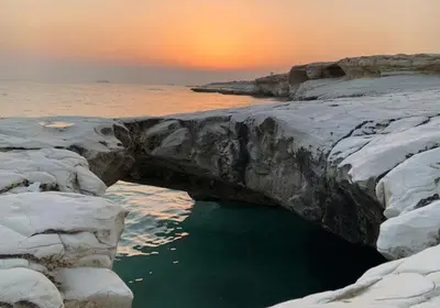 a hole in the rocks in the water with the sunset at Governors Beach Costas Apts in Governors Beach