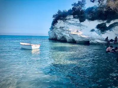 a boat in the water next to a cliff at Governors Beach Costas Apts in Governors Beach