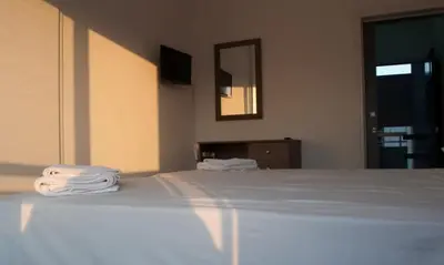 a bedroom with a bed with white sheets and a mirror at St. George Rent Rooms in Larnaka