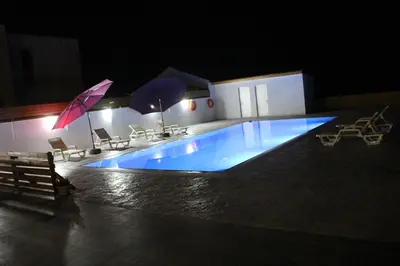 a large blue swimming pool at night with umbrellas at BerryRose Villa in Pervolia