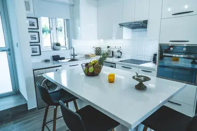 a white kitchen with a island with a bowl of fruit on it at Andreotis Villas in Protaras