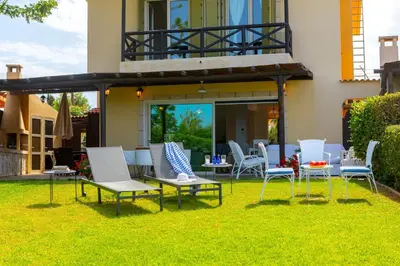 a patio with white chairs and tables on the grass at Protaras Sirina Waterfront Villa in Protaras