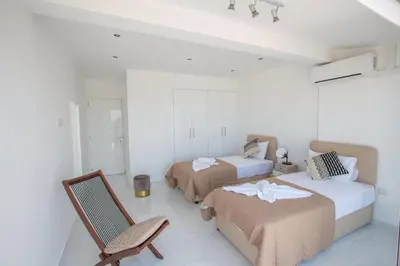 a white room with two beds and a chair at Rio Luxury Apartment in Ayia Napa