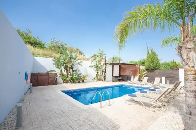 a swimming pool with chairs and a palm tree at Villa To Perivoli in Protaras
