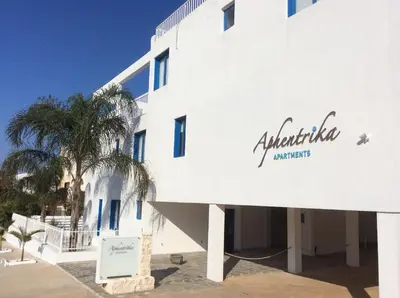 a white building with a palm tree in front of it at Aphentrika Apartments in Protaras