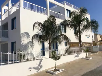 a white building with palm trees in front of it at Aphentrika Apartments in Protaras