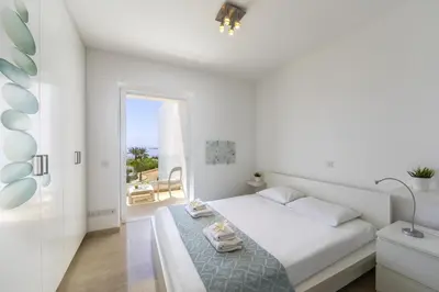 a white bedroom with a bed and a balcony at Protaras Villa Kalena Seafront in Protaras