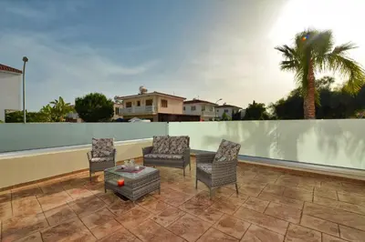 a patio with chairs and a table and a palm tree at Nissi Martha Apartment in Ayia Napa