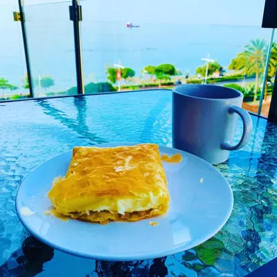 a piece of cake on a plate on a table with a cup at Thalassa Sea View Suite in Limassol
