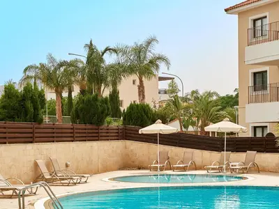 a swimming pool with chairs and umbrellas next to a building at Kyklades Angie Resort in Protaras