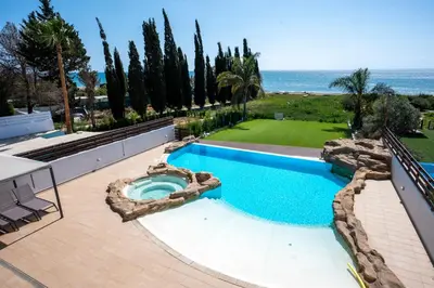a swimming pool next to a lawn with trees and the ocean at AAA SEAVIEW PANORAMA in Pervolia