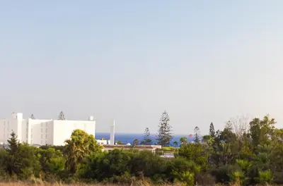 a large white building with trees in the foreground at Nissi Elena -Sunshine Apt in Ayia Napa