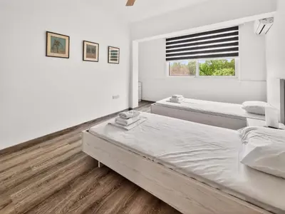 a white bedroom with two beds and a window at Sofia's Seaview in Protaras