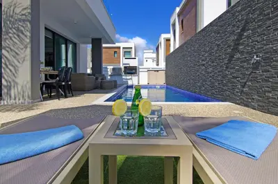 a table with a bottle and glasses on it next to a pool at Villa Mey in Protaras