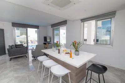 a kitchen and living room with a table and stools at Fig Tree Bay Residences 1 Lantiana Villa in Protaras