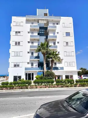 a large white building with palm trees in front of it at 13 Sandy Beach Mackenzie in Larnaka
