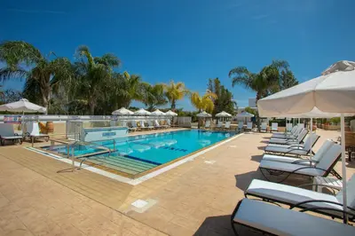 a swimming pool with lounge chairs and umbrellas at Flouressia Gardens in Protaras