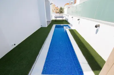 a swimming pool with blue tiles and green grass at Villa Lynn Boutique Beachfront in Ayia Napa