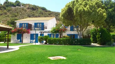 a white house with blue windows and a green yard at Hylatio Tourist Village in Pissouri
