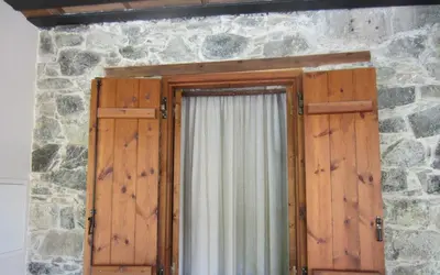 a window with wooden doors in a stone wall at Ayios Andronikos Agrotourism House in Kalopanayiotis