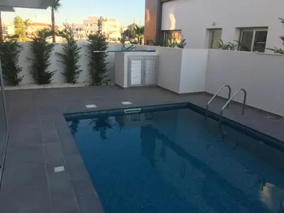 a swimming pool in front of a white wall and a building at Mobina Villas in Larnaka
