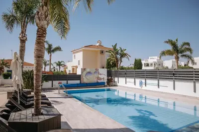 a swimming pool with palm trees in front of a house at Sunset Villa private complex heated pool in Ayia Napa