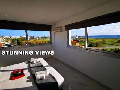 a bedroom with a bed and two windows with the ocean at Nissi Avenue Suites in Ayia Napa