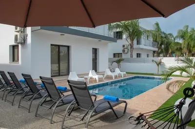 a pool with chairs and a table and an umbrella at Villa Fortuna in Ayia Napa