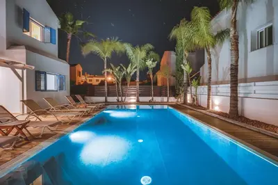 a swimming pool with palm trees and a building at Amphitrite Villa in Paralimni