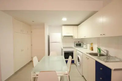a kitchen with white cabinets and a table and a sink at Napa Blue Apartment, XXL Pool,in Hearth of Ayia Napa in Ayia Napa