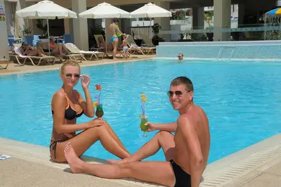 a man and woman in bathing suits sitting next to a swimming pool at Nelia Gardens in Ayia Napa