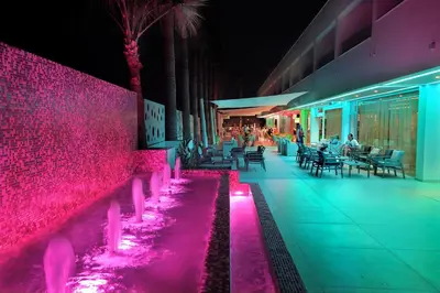 a resort with a pink wall and tables and chairs at Nelia Beach Hotel & Spa in Ayia Napa