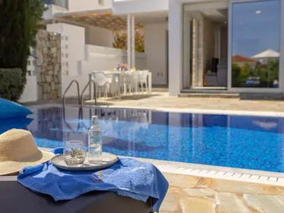 a table with a bottle and glasses next to a swimming pool at Villa Zoe in Protaras