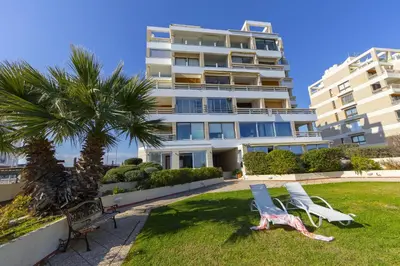 a building with two lawn chairs and a palm tree at Mackenzie Castella Beachfront Suite in Larnaka