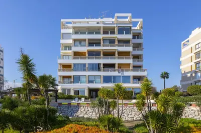a tall white building with palm trees in front of it at Mackenzie Castella Beachfront Suite in Larnaka