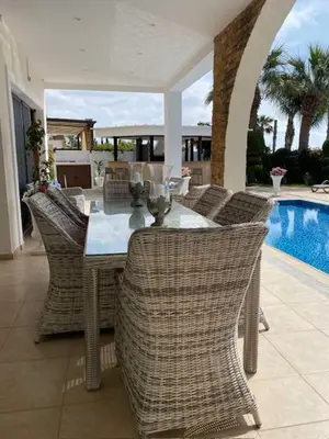 a dining table with wicker chairs next to a pool at Ionion Beachfront Villa in Ayia Napa