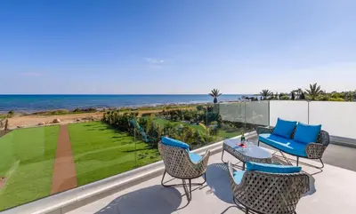 a patio with chairs and tables and the ocean at Serenity Seafront Villa in Ayia Napa