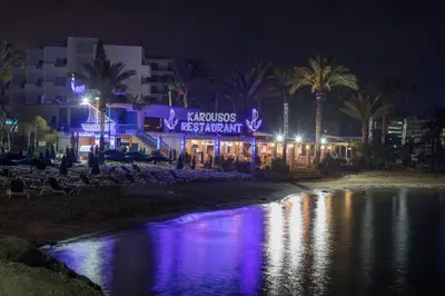 a building with a sign on the beach at night at Karousos Beach Rooms in Ayia Napa