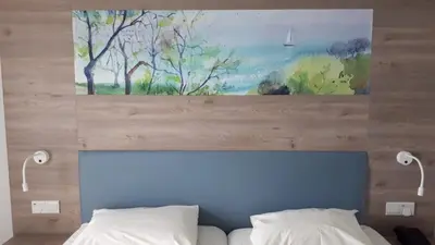 a painting above a bed with two white pillows at Karousos Beach Rooms in Ayia Napa