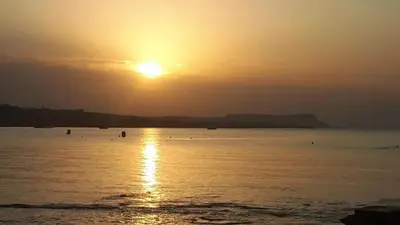 a sunset over the ocean with people in the water at Karousos Beach Rooms in Ayia Napa