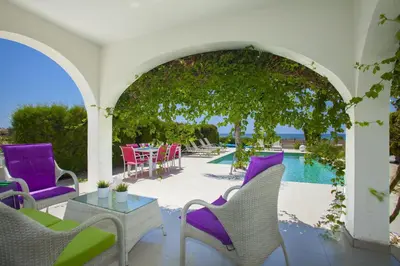 a patio with purple chairs and a table and a pool at Ayia Thekla Seafront Villa Lavender in Ayia Napa