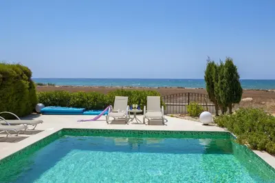 a swimming pool with chairs and a table and the ocean at Ayia Thekla Seafront Villa Lavender in Ayia Napa