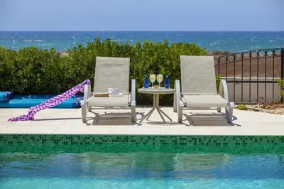 two chairs and a table next to a swimming pool at Ayia Thekla Seafront Villa Lavender in Ayia Napa