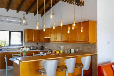 a kitchen with wooden cabinets and a counter with white chairs at Ayia Napa Ammos Sea View Villa in Ayia Napa