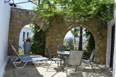 a patio with a table and chairs and a stone wall at George Houses in Pendakomo