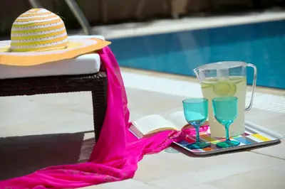 a hat and two glasses and a book next to a pool at Protaras Villa Michelle 9 in Protaras