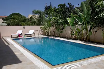 a swimming pool with two chairs next to a building at Protaras Villa Michelle 9 in Protaras